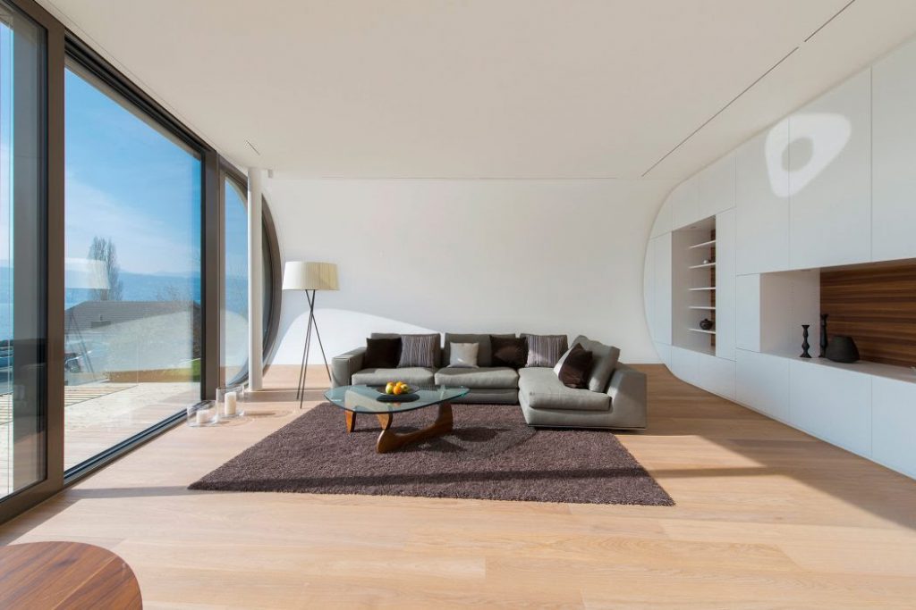 grey sofa seats with brown floor carpate on wooden floor and white color walls