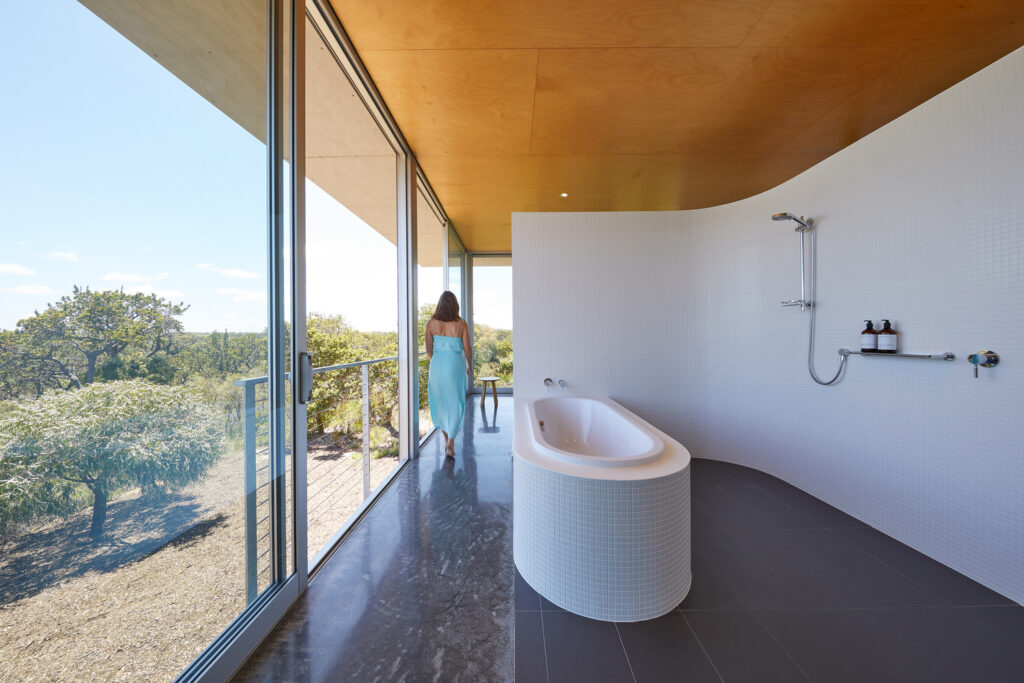 lady in bath, white bath tub, curve shower wall, italian flooring, wooden ceiling,