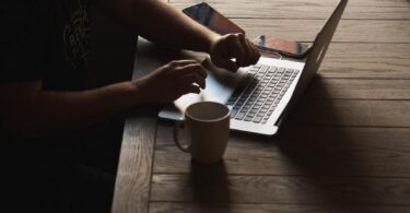 A person sitting at their work desk with their laptop set up and a mug placed next to it.