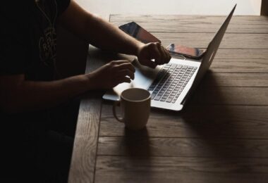 A person sitting at their work desk with their laptop set up and a mug placed next to it.